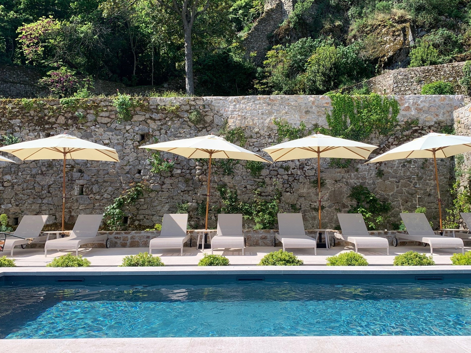 Pool area with umbrellas and lounge chairs along stone wall